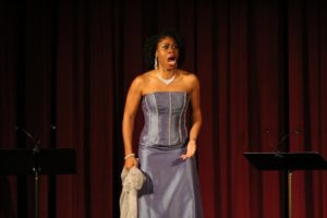 Chrystal E. Williams as Charlotte in the 2017 joint concert production of Werther by Baltimore Concert Opera and Opera Delaware. Photo by Courtney Kalbacker. Williams is pictured here in a periwinkle gown, dangling diamond earrings, ruby ring, diamond bracelet, and a shimmery silver shawl balled in her right fist. She looks fierce, her mouth open in singing.